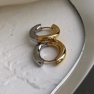 Detail of two-tone gold and silver hoop earrings on a textured cream surface