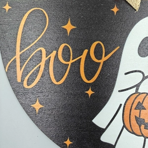Close-up of wooden Boo door sign with ghost and pumpkin printed details for Halloween decor