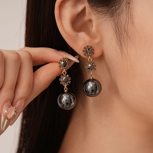 Détail de boucle d'oreille pendante vintage dorée et gris foncé avec strass et perle