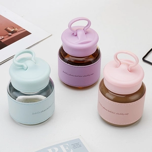 Three colorful chubby glass cups with silicone lids and phone holder sleeves on a white desk