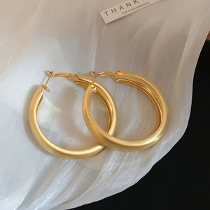 Detail of large gold hoop earrings with matte finish on soft white silk background