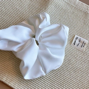 Close-up of a large white silk scrunchie with soft pleats on a textured fabric background