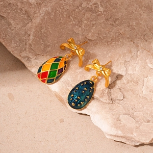 Detailed shot of vintage insect bow earrings with colorful enamel egg pendants on stone