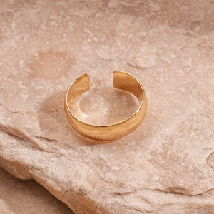 Close-up of a gold adjustable open ring on natural light brown textured stone surface