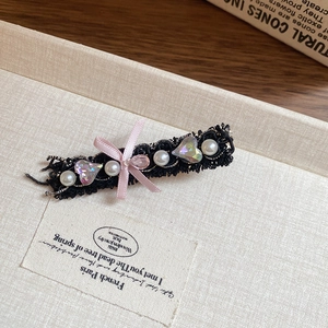 Detailed view of pink bow hair clip with pearls and heart crystals on black lace