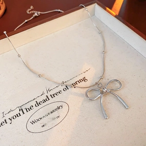 Detailed macro of a silver bow pendant on a beaded snake chain with minimalist aesthetic