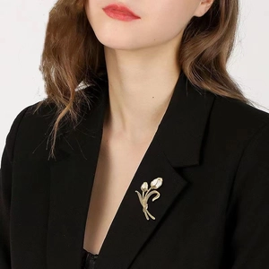 Detailaufnahme der goldenen Brosche mit weißen Callas an einem schwarzen Revers