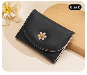 Detail of black pebbled leather tri-fold wallet featuring a cute 3D pink daisy floral charm