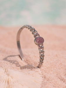 Detail view of silver curb chain bracelet with pink zircon plate on a white coral beach