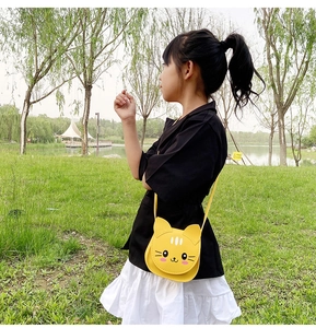Little girl wearing a yellow cartoon cat crossbody bag outdoors on the grass