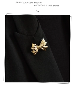 Close-up of a polished golden bow brooch pinned on a black suit lapel with shiny finish