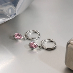 Detailweergave van zilveren oorringen met roze traanvormige edelstenen op glanzend oppervlak