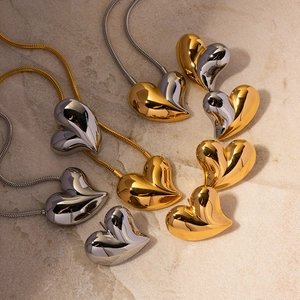 Polished 18K gold and silver chunky heart earrings and necklace on beige stone pedestal