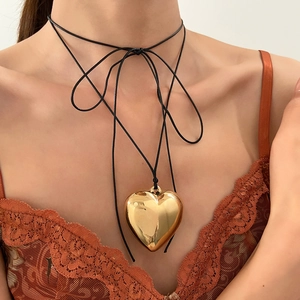Close-up of polished gold heart pendant necklace with black thin cord on model