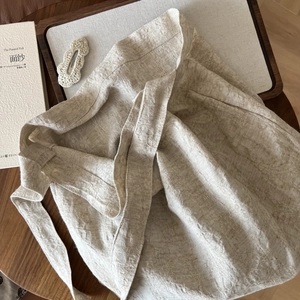 Detailed close-up of natural beige linen fabric texture and long tie strap on a crossbody bag