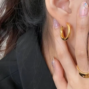 Close-up of minimalist golden titanium hoop earrings and matching ring on a model