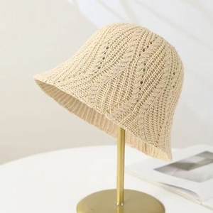 Beige openwork knit bucket hat with textured crochet pattern on gold metal stand