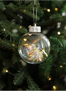 Close-up of clear holographic Christmas tree ball hanging on pine branches with warm lights