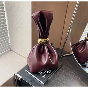 Detail of burgundy drawstring bucket bag with a gold metal ring on a book base