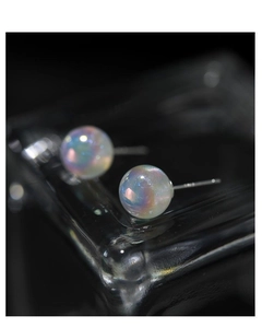 Macro shot of iridescent mermaid pearl stud earrings with a silver pin on black reflective base