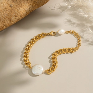 Detail of gold chunky chain bracelet with white baroque pearls on a stone background