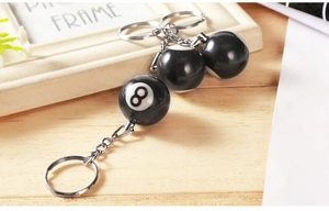Detailed close-up of three black number 8 resin billiard ball keychains on a wooden desk