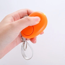 Detail of orange safety alarm with LED light held in hand showing pull ring keychain