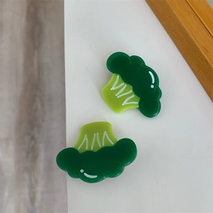 Detail of two green broccoli hair clips featuring white outlines and a cute smiley face
