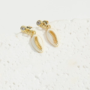 Detailed close-up of shell-shaped gold earrings with rhinestones on a textured stone