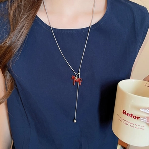 Detail of a minimalist necklace with a red horse pendant on a silver snake chain
