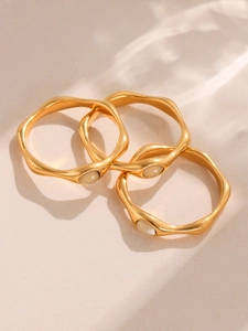 Detail of three stacked gold wavy rings featuring elegant cream stone inlays on textured background