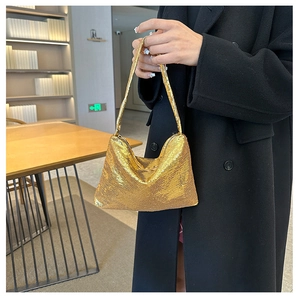 Gros plan d'un sac hobo à paillettes dorées tenu par un mannequin dans un café chic
