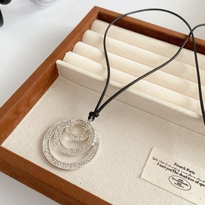 Detailed view of layered circular pendant with crystals on a black cord in a jewelry box