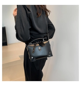 Detail of black leather crossbody bag with silver studs and skull emblem worn by model
