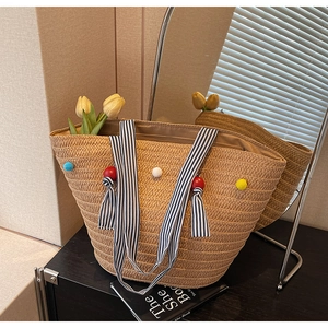 Detail of hand-woven straw tote with colorful pom-poms and striped fabric handles