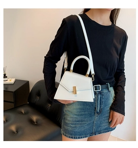 Chic white trapezoid handbag with gold buckle shown on a model in a minimalist setting