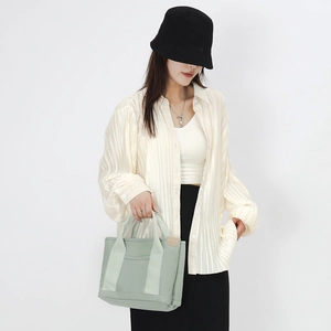 Close-up of light green canvas tote bag with textured ribbon handles and leather side detail