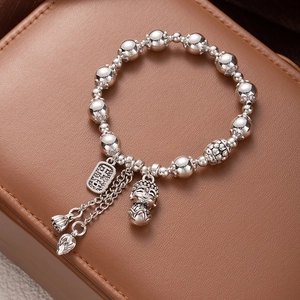 Macro shot of silver beaded bracelet featuring carved square charm and lotus pendants