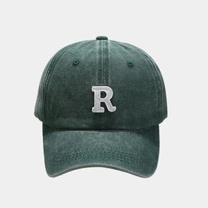 Detailed close-up of white embroidered letter R on washed dark green baseball cap