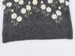 Dettaglio del gilet in maglia grigio scuro con margherite bianche e fiori 3D fatti a mano