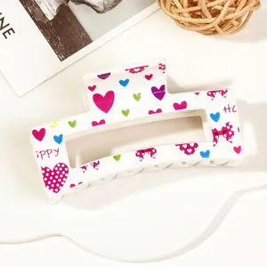 Detail of white rectangular hair claw clip with colorful heart and bow print patterns
