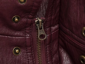 Macro detail of vintage bronze zipper and studs on dark burgundy textured PU leather jacket