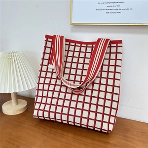 Detail of red and white checkered knit tote bag on wooden table with a cozy lamp