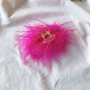 Detailed view of a pink ostrich feather hair claw clip on a white fabric background