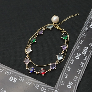 Double-layered gold bracelet featuring vibrant oval gemstones and a white pearl charm