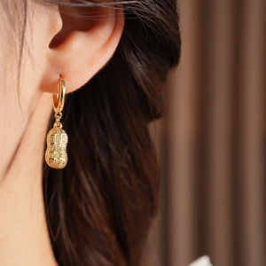 Close-up of a gold-plated peanut drop earring worn on a model in a warm setting