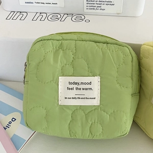 Close-up of mint green quilted floral pouch featuring a minimalist canvas label and zipper