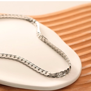 Detail shot of a silver Cuban chain necklace on a white tray with wood texture background