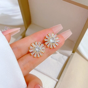 Golden sunflower earrings with clear zircon stones shown held in hand against a gift box