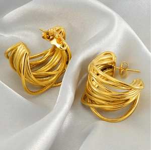 Macro detail of gold multi-layered intertwining hoop earrings on white silk fabric